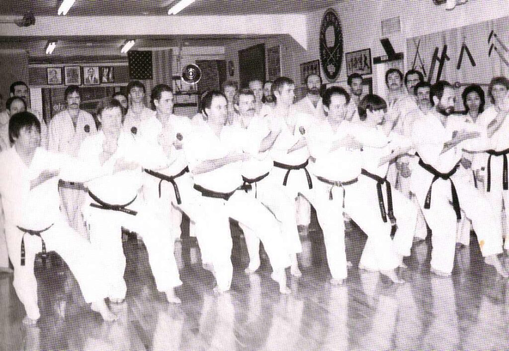 A photo of a group of karate-ka in the Ueshiro Shorin Ryu Hombu Dojo (headquarters) in New York, including Master Ansei Ueshiro on the far left, and Hanshi Robert Scaglione on the far right.